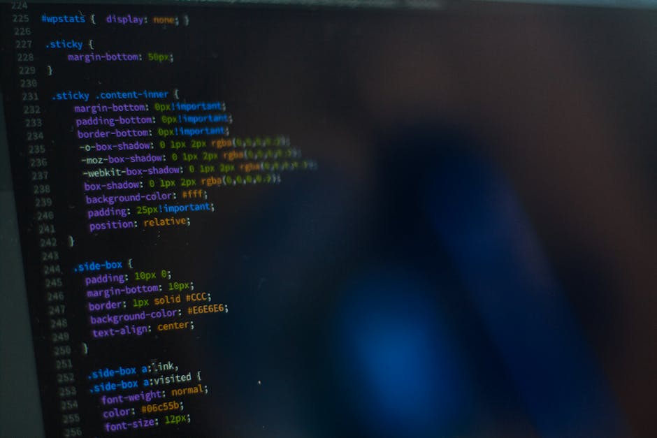 A photograph of a computer screen displaying lines of multicoloured code on a dark background. The code includes various syntax elements in red, green, blue, and purple, with some numerical values and